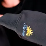 Canguro con capucha de diseño bicolor, con cuerpo principal en color negro y mangas en color gris. Presenta un bolsillo frontal tipo canguro, puños y ruedo acanalados, y un pequeño logo bordado en el pecho.