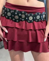 Cinturón de cuero sintético negro compuesto por piezas circulares unidas, decoradas con ojalillos metálicos y apliques centrales en forma de sol.