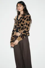 Chaqueta de punto con textura suave, cuello redondo y manga larga. Presenta un diseño de estampado animal print en tonos marrones y negros, con cierre frontal de botones.