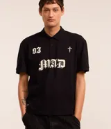 Remera de corte boxy confeccionada en algodón, con cuello polo y cierre frontal de botones. Presenta un diseño estampado en el frente con el número 93, una cruz y la palabra MAD en tipografía gótica.