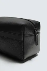 Neceser de piel negra con acabado abatanado, cierre de cremallera en el compartimento principal y un bolsillo interior también con cremallera. Incluye un asa de mano en un lateral.