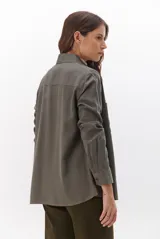 Camisa beige de manga larga, con cuello clásico, botones marrones y dos bolsillos frontales. Presenta costuras decorativas en contraste.