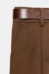 Pantalón tiro bajo color marrón, de corte globo y pernera recta con raya marcada al frente. Incluye trabillas y un cinturón marrón oscuro con hebilla metálica.