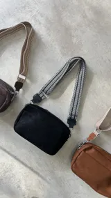 Bandolera negra de gamuza sintética con correa ancha de tela con diseño geométrico en blanco y negro.