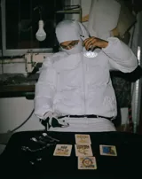 Campera puffer negra con capucha, cierre frontal con botones a presión y cordones ajustables en la cintura. Presenta un estampado gráfico circular con el número 27 en el pecho.