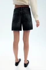 Bermuda de tiro medio confeccionada en denim de color negro gastado, con diseño de cinco bolsillos, trabillas para cinturón y cierre frontal con cremallera y botón metálico.