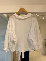Camisa blanca de lino con mangas abullonadas y detalles de bordado inglés en las mangas y en los laterales. Presenta cuello camisero, cierre frontal con botones y tiritas para atar en el frente.