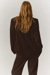 Blazer de color marrón oscuro, de corte ligeramente largo, con solapas de muesca y cierre de doble botonadura con botones oscuros. Presenta hombreras y bolsillos delanteros ribeteados con solapa.