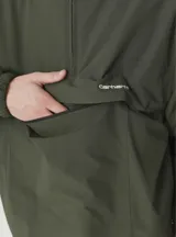 Campera tipo windbreaker de estilo pullover, color verde militar, con capucha ajustable, cierre frontal parcial y bolsillo tipo canguro con cierre. Presenta el logo de la marca bordado en el pecho.