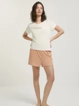 Pijama compuesto por una remera de algodón color crema con cuello redondo y estampa frontal con texto, y un short de tela rayada en tonos salmón con cintura elástica.