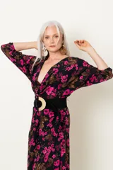 Vestido midi negro con estampado floral fucsia y marrón, escote en V cruzado, mangas largas y cinturón ancho negro con hebilla circular.