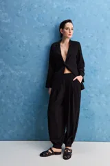 Pantalón negro de tiro alto y calce holgado, con pierna amplia, bolsillos laterales y puños ajustados con botones en los tobillos.