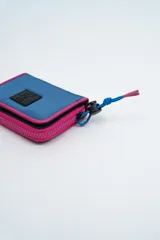 Billetera de diseño deportivo en color azul con bordes en fucsia. Presenta un parche frontal con el logo de la marca y un cierre con tirador de cordón ajustable.