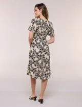 Vestido midi de rayón en color beige con estampado floral en negro, escote en V, pechera con punto smock, mangas cortas acampanadas con detalle de galón y falda evasé con volado en el ruedo. Incluye lazo textil ajustable en la cintura.