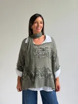 Sweater de punto color verde oliva con diseño de paneles horizontales de encaje floral, corte holgado y mangas tres cuartos. Incluye una bufanda del mismo tono y tejido, y se presenta superpuesto sobre una camisa blanca de cuello clásico.