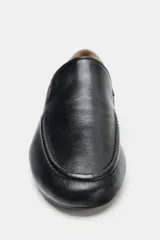 Zapato tipo mocasín de piel negra con copete subido, punta redonda y suela plana.