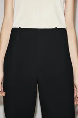 Pantalón de tiro medio con cintura con trabillas, detalle de raya planchada y bajo con aberturas laterales. Cierre frontal con cremallera, botón y ganchos metálicos.
