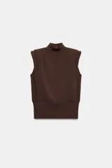 Top de punto color marrón oscuro, con cuello subido, sin mangas, hombreras y detalles de pliegues. Cuenta con diseño de espalda descubierta y cierre trasero con botones.