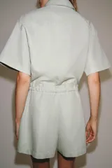 Mono corto de Zara Woman Collection color verde menta, confeccionado en mezcla de algodón y lino. Presenta cuello solapa, manga corta, cierre frontal con botones, bolsillos de plastrón con solapa en el pecho y cintura ajustable con lazo.