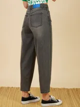 Jean de corte mom fit en color gris oscuro con efecto lavado. Presenta tiro alto, cierre frontal con botón metálico y costuras verticales en el frente de las piernas.