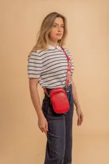 Bandolera compacta color rojo con textura de cuero, correa regulable y desmontable con diseño de rayas rojas y blancas. Cuenta con bolsillos frontales y cierre, interior forrado en tela.