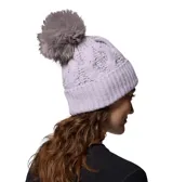 Gorro de lana tejido con diseño de ochos, color lila, con pompón de pelo sintético en tono beige y etiqueta metálica de la marca Columbia en el borde.