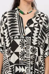 Camisa oversize de manga corta, con diseño estampado geométrico en blanco y negro, escote en V con cuello mao y cierre frontal con botones.