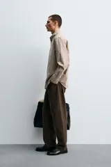 Camisa de algodón de manga larga, cuello abotonado y cierre frontal de botonadura. Presenta un patrón de cuadros pequeños en tonos beige, marrón y blanco.