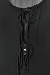 Camisa de viscosa con cuello redondo y escote en pico ajustable mediante lazadas. Presenta cierre frontal con botones, mangas largas con terminación evasé y detalle de volantes en el mismo tejido.