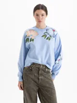 Buzo oversize de cuello redondo, color celeste, con estampado floral en la parte superior delantera y en una de las mangas.