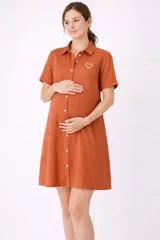 Camisa maternal color naranja óxido, de viscosa suave y liviana, con cuello camisero, mangas cortas y cierre frontal abotonado. Presenta un bordado de corazón blanco en el pecho y bolsillos laterales.