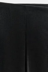 Pantalón de tiro medio con corte tipo ballon, bolsillos delanteros y detalle de pinzas. Cuenta con cierre frontal de cremallera y gancho metálico.