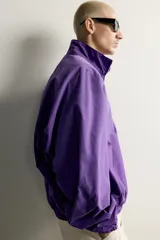 Cazadora relaxed fit de denim de algodón en color violeta, con efecto lavado, cuello alto, cierre frontal de cremallera y bolsillos en las costuras laterales. Presenta puños y dobladillo elásticos.