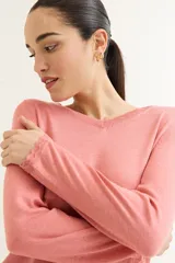 Sweater rosado de tejido de punto con escote en V y mangas largas con puños acanalados. El ruedo también es acanalado y presenta un detalle de crochet.