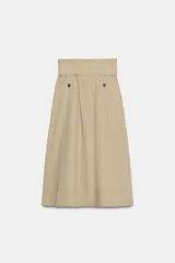 Falda midi color beige confeccionada en hilatura con mezcla de algodón. Presenta tiro medio, cintura con trabillas, bolsillos laterales ocultos en costura y cinturón del mismo tejido. Su diseño incluye un bajo acabado en línea evasé y cierre lateral con cremallera.