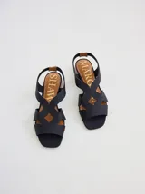 Sandalia de diseño minimalista con tiras anchas de neopreno negro, taco bajo de madera y detalle de tira trasera en color suela.