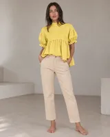 Blusa blanca de lino, con cuello alto, mangas cortas abullonadas con puños con volados y diseño amplio con frunce bajo el busto.