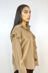 Camisa de pana fina color beige, con volados decorativos en los hombros y a lo largo de la botonadura frontal. Presenta cuello clásico, mangas largas con puños y cierre mediante botones dorados.