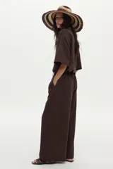 Pantalón de lino marrón de corte ancho y relajado, con pinzas frontales, bolsillos y lazo ajustable en la cintura.