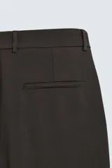 Pantalón de corte relajado con pliegues frontales, bolsillos laterales y bolsillos traseros de vivo. Presenta cierre frontal con cremallera y botón.