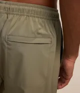 Bermuda de baño color beige con cintura elástica, cordón de ajuste negro en contraste, bolsillos laterales y un pequeño tag engomado en el bajo.