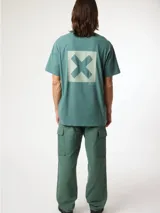 Camiseta de manga corta color verde azulado, corte holgado, con un pequeño estampado cuadrado con una 'X' en el pecho.