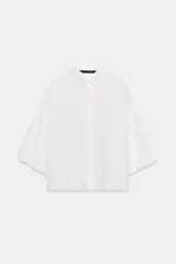 Camisa blanca de cuello solapa y mangas cortas abullonadas tipo globo, con bajo recto y cierre frontal de botonadura oculta bajo tapeta.