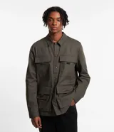 Campera masculina color verde oliva, estilo parka, confeccionada en sarga de algodón. Cuenta con cuello con solapa, cierre con botones, manga larga y múltiples bolsillos táticos delanteros.