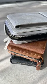 Cartera portacelular con correa larga, cierre con cremallera y solapa con broche imantado.