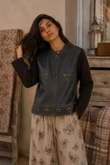 Campera bicolor con frente de cuero sintético gris oscuro y mangas y espalda de tejido marrón. Presenta cuello mao con broche a presión, cierre frontal y bolsillos con cierre en el pecho. El ruedo está decorado con ojalillos metálicos aplicados.