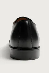 Zapato de vestir tipo derby de color negro, confeccionado en cuero con forro y plantilla de cuero, horma cuadrada y suela con ligero tacón.