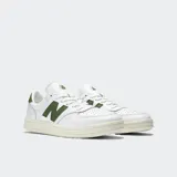 Championes New Balance modelo CT500, color blanco con logo 'N' y detalles en verde oliva. Tienen una silueta de corte bajo inspirada en el tenis, con parte superior de cuero y suela de goma color crema.