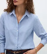Camisa de tricolina de algodón con estampa de rayas celestes y blancas, cuello solapa, abotonado frontal y mangas largas. Marca Cortelle.