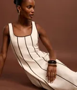 Vestido largo evasê sin mangas de color beige, con escote cuadrado y costuras verticales con bies en tono contrastante oscuro.
